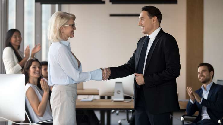 Executive older male and middle aged female executive shake hands congratulating with promotion